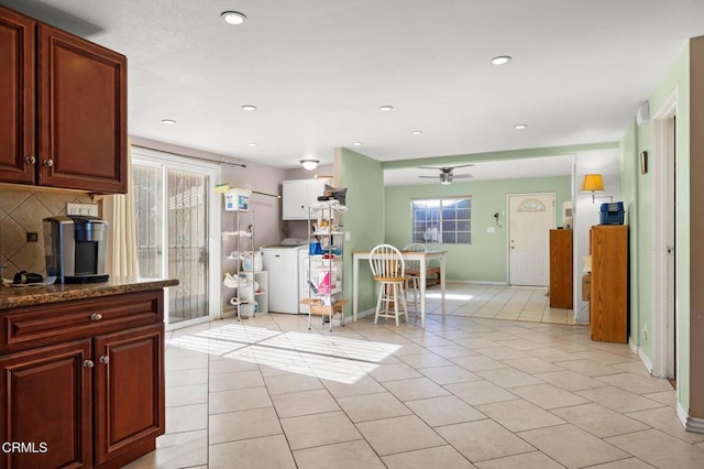 kitchen featuring backsplash, dark stone counters, ceiling fan, light tile patterned floors, and washer / clothes dryer