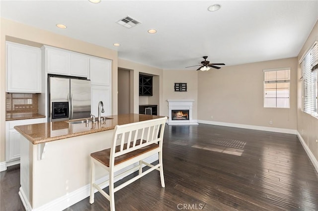 kitchen with stainless steel refrigerator with ice dispenser, sink, a center island with sink, and white cabinets