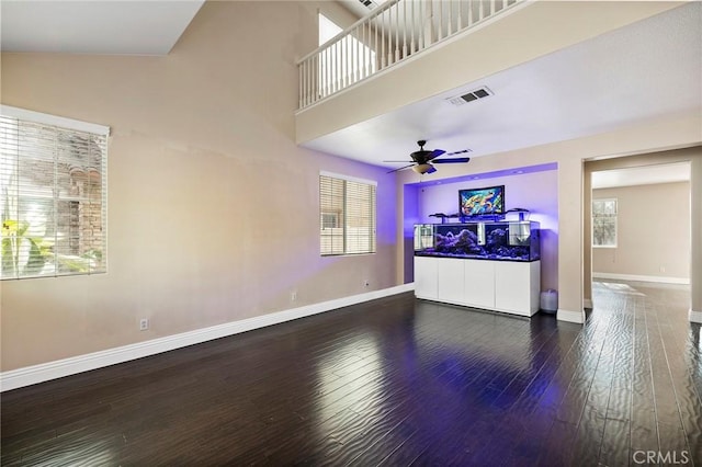 living room with dark hardwood / wood-style flooring, ceiling fan, a healthy amount of sunlight, and a high ceiling