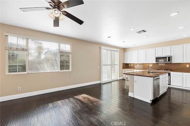 kitchen with white cabinetry, appliances with stainless steel finishes, dark hardwood / wood-style flooring, a kitchen island with sink, and backsplash