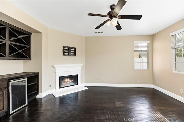 unfurnished living room featuring wood-type flooring, indoor bar, beverage cooler, and ceiling fan