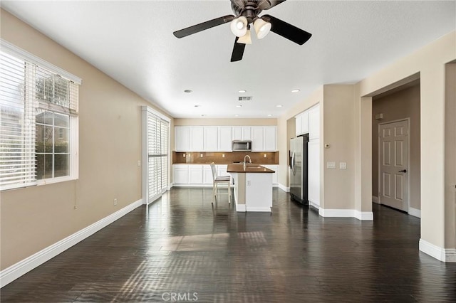 kitchen featuring dark wood-type flooring, appliances with stainless steel finishes, white cabinetry, an island with sink, and decorative backsplash