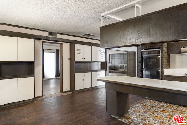 kitchen featuring white cabinets, dark hardwood / wood-style flooring, black double oven, and a textured ceiling