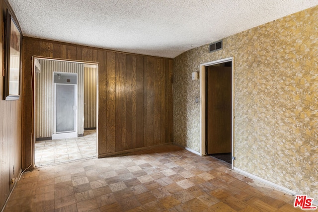 spare room featuring a textured ceiling and wooden walls