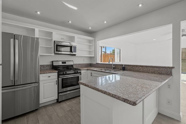 kitchen with stone counters, white cabinets, sink, kitchen peninsula, and stainless steel appliances