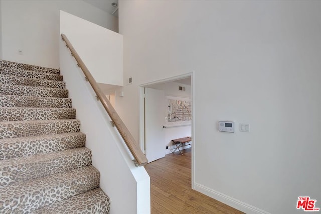 stairway featuring wood-type flooring and a towering ceiling