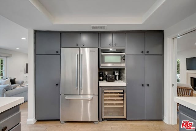 kitchen with beverage cooler, stainless steel appliances, light hardwood / wood-style floors, backsplash, and a raised ceiling