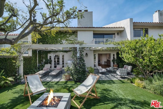 rear view of property featuring a balcony, a patio area, a yard, and an outdoor living space with a fire pit