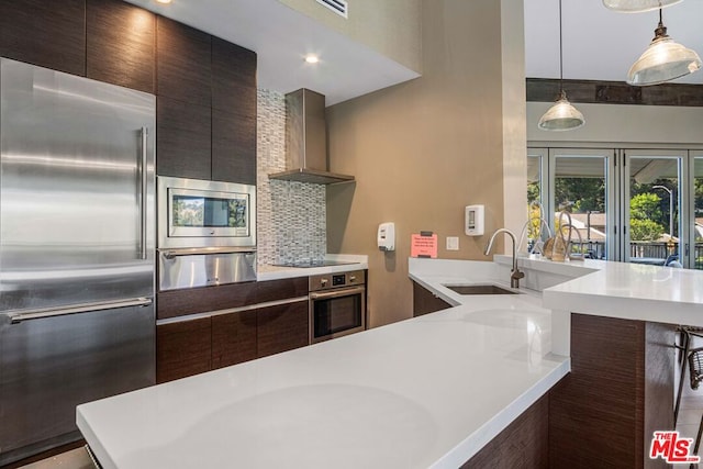 kitchen with decorative light fixtures, wall chimney range hood, stainless steel appliances, sink, and backsplash