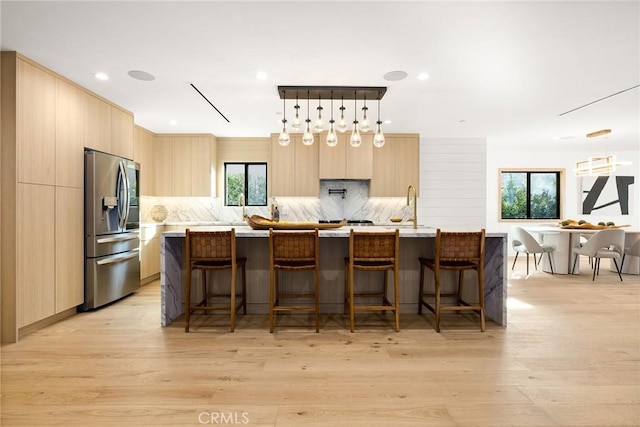 kitchen featuring decorative light fixtures, a center island with sink, light brown cabinets, and stainless steel refrigerator with ice dispenser