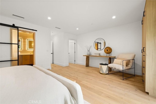 bedroom with connected bathroom, light hardwood / wood-style floors, and a barn door