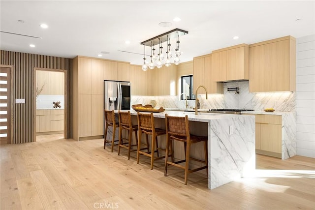 kitchen featuring a kitchen breakfast bar, light brown cabinets, hanging light fixtures, a center island with sink, and light hardwood / wood-style flooring