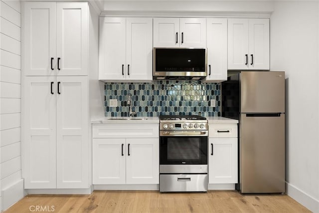 kitchen featuring tasteful backsplash, white cabinetry, sink, stainless steel appliances, and light hardwood / wood-style flooring