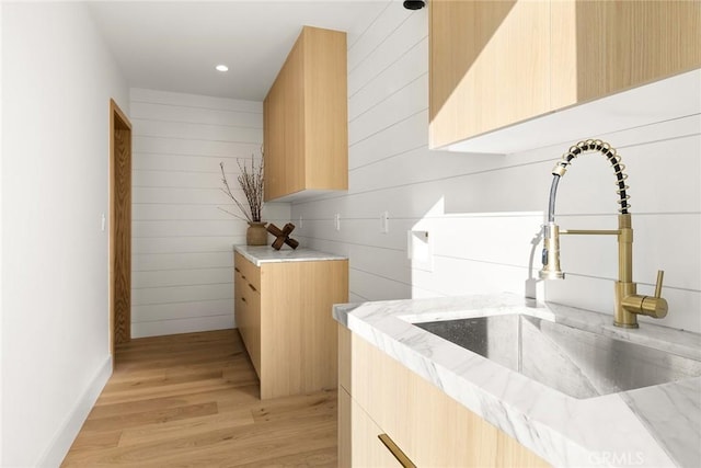 kitchen featuring modern cabinets, light stone countertops, light wood-type flooring, light brown cabinets, and a sink