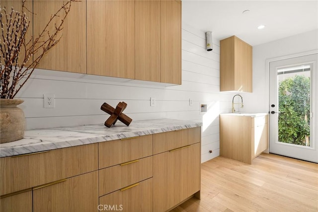 kitchen with modern cabinets, light stone counters, light wood-type flooring, a sink, and recessed lighting