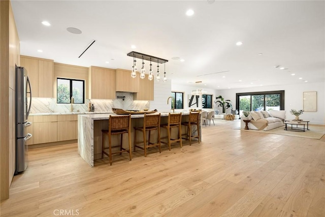 kitchen featuring a breakfast bar, light hardwood / wood-style flooring, light brown cabinets, a center island with sink, and backsplash