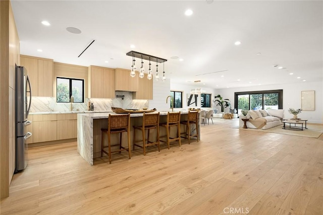 kitchen with light wood finished floors, modern cabinets, freestanding refrigerator, light brown cabinets, and a sink