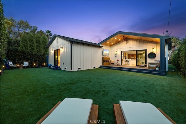 back house at dusk featuring an outbuilding and a lawn