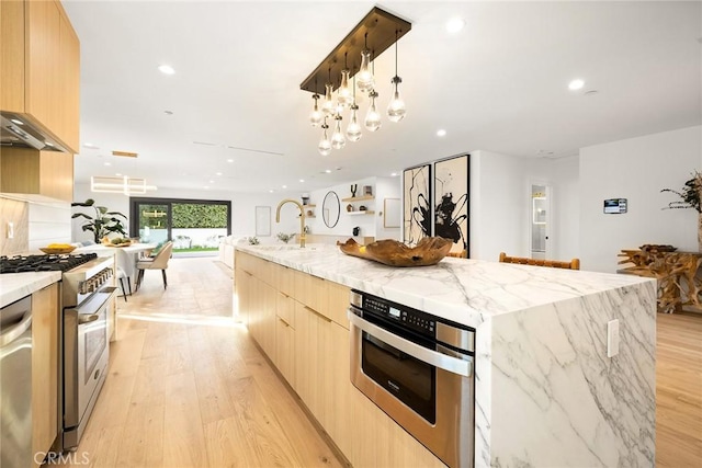 kitchen featuring sink, appliances with stainless steel finishes, hanging light fixtures, light stone counters, and a large island with sink