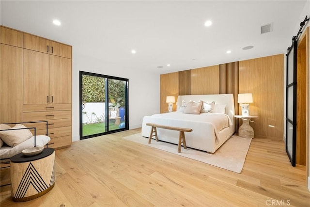 bedroom with a barn door, wood walls, visible vents, access to exterior, and light wood finished floors