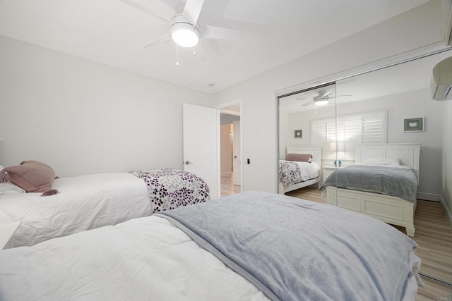 bedroom with a wall mounted air conditioner, light hardwood / wood-style flooring, a closet, and ceiling fan