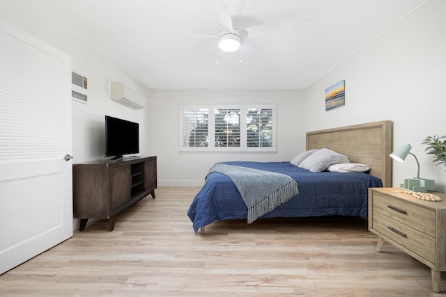 bedroom with light hardwood / wood-style flooring, ceiling fan, and an AC wall unit