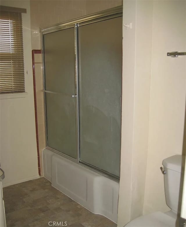 bathroom featuring toilet and combined bath / shower with glass door