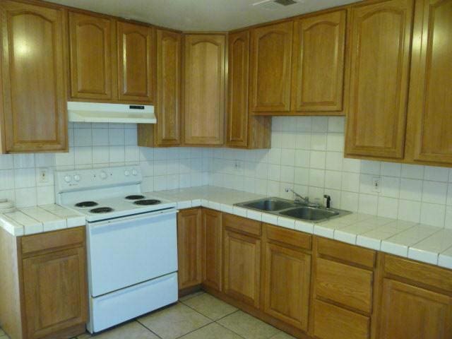 kitchen with tile counters, light tile patterned floors, electric range, and sink