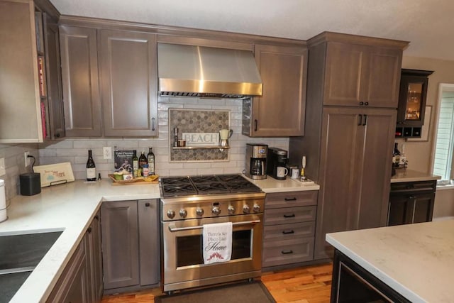 kitchen featuring wall chimney range hood, decorative backsplash, light hardwood / wood-style flooring, and high end stainless steel range oven