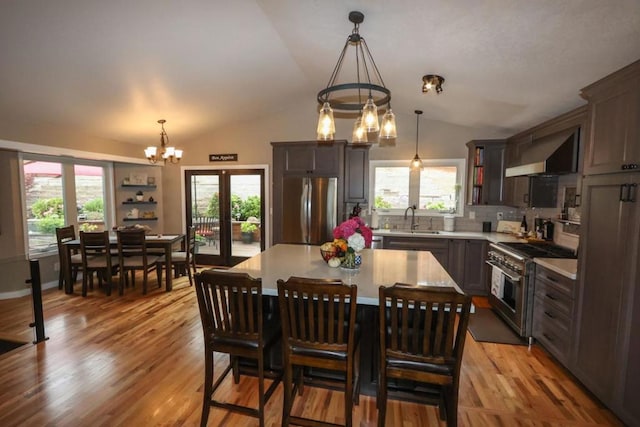 kitchen with wall chimney range hood, sink, appliances with stainless steel finishes, an inviting chandelier, and a center island