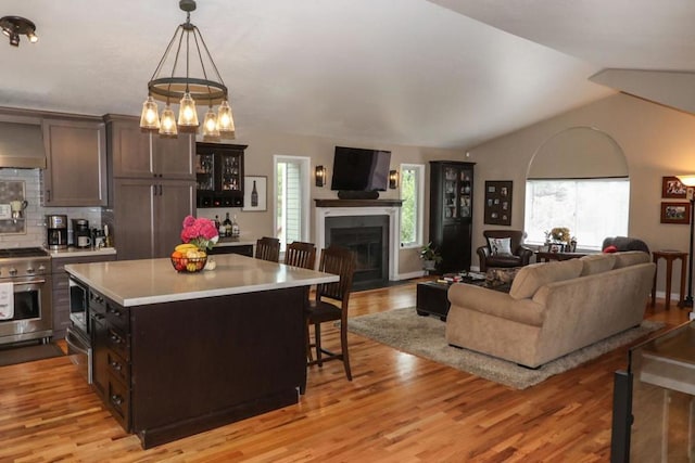 kitchen featuring a breakfast bar area, custom exhaust hood, hanging light fixtures, dark brown cabinetry, and stainless steel appliances