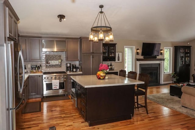 kitchen featuring wall chimney exhaust hood, a breakfast bar, hanging light fixtures, appliances with stainless steel finishes, and a kitchen island