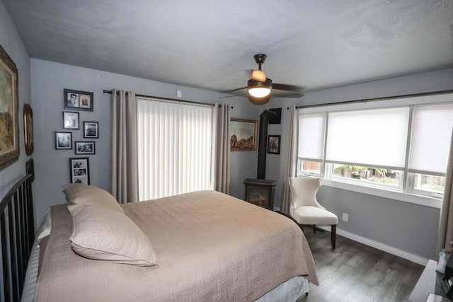 bedroom with dark hardwood / wood-style floors, a wood stove, and ceiling fan