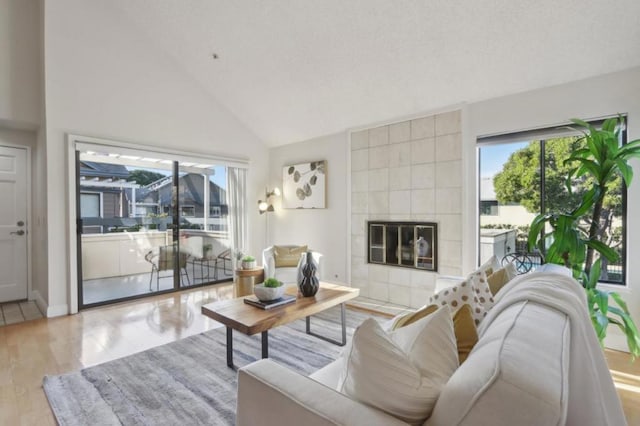 living room with high vaulted ceiling, a tile fireplace, and light hardwood / wood-style floors