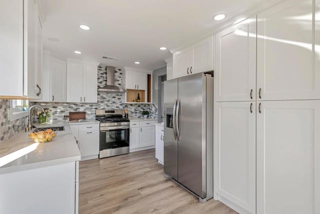 kitchen featuring appliances with stainless steel finishes, decorative backsplash, wall chimney exhaust hood, white cabinets, and sink