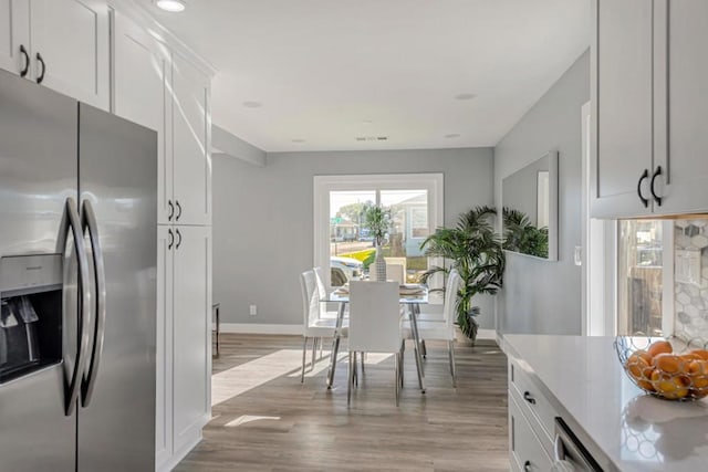 kitchen with stainless steel refrigerator with ice dispenser, light hardwood / wood-style floors, and white cabinets