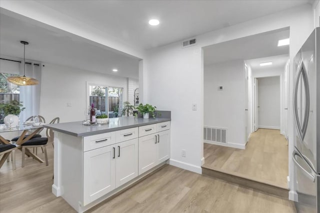 kitchen with pendant lighting, white cabinetry, stainless steel fridge, kitchen peninsula, and light hardwood / wood-style flooring