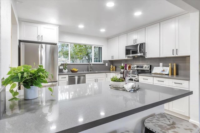 kitchen featuring a kitchen bar, white cabinetry, stainless steel appliances, sink, and kitchen peninsula