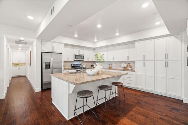 kitchen with light stone countertops, white cabinets, appliances with stainless steel finishes, a kitchen bar, and a center island with sink