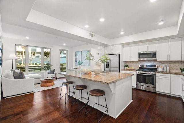 kitchen featuring a breakfast bar area, stainless steel appliances, light stone countertops, a kitchen island, and white cabinets