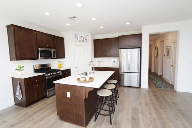 kitchen featuring sink, a breakfast bar area, stainless steel appliances, a center island with sink, and light wood-type flooring