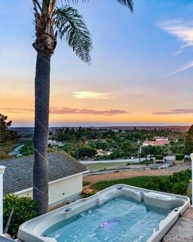 pool at dusk with an outdoor hot tub