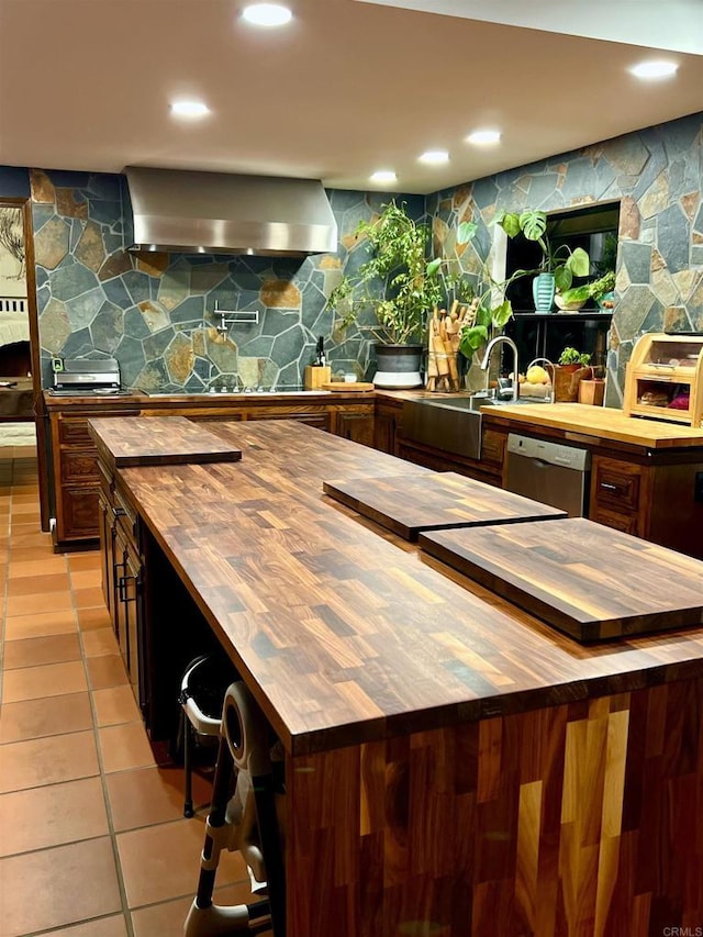 kitchen featuring dishwasher, light tile patterned floors, wooden counters, dark brown cabinetry, and wall chimney range hood