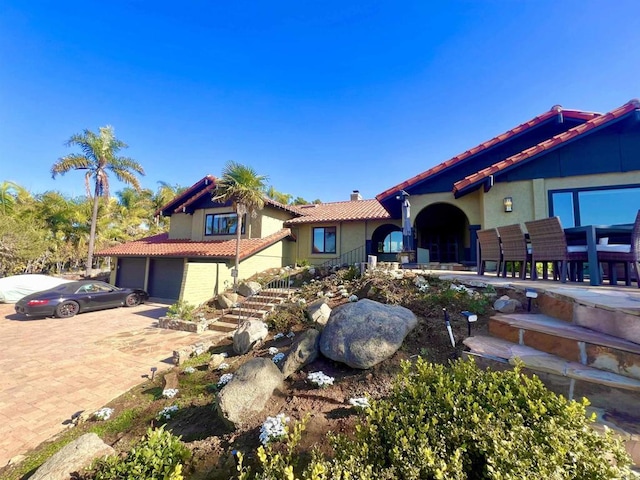mediterranean / spanish house with driveway, a tile roof, a garage, stucco siding, and a chimney