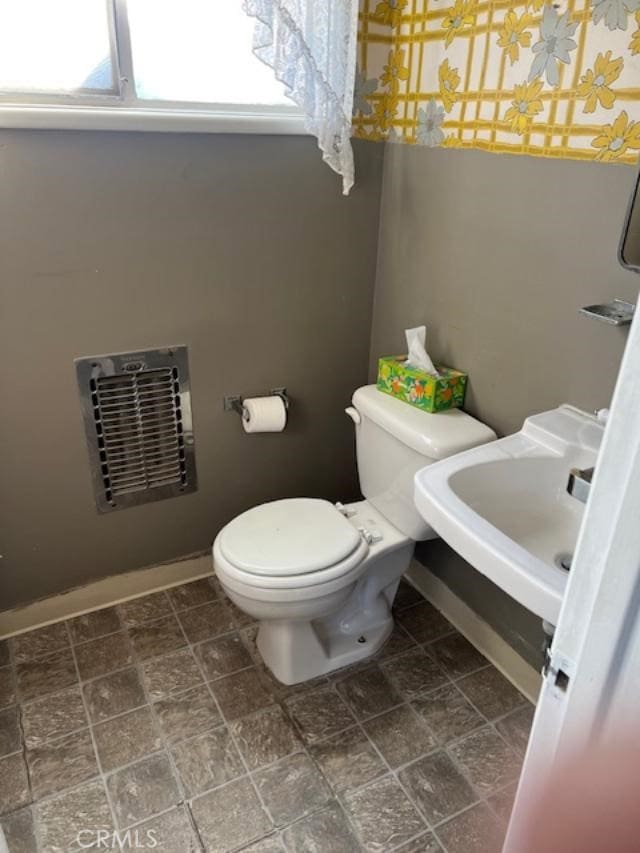 bathroom featuring heating unit, toilet, and sink