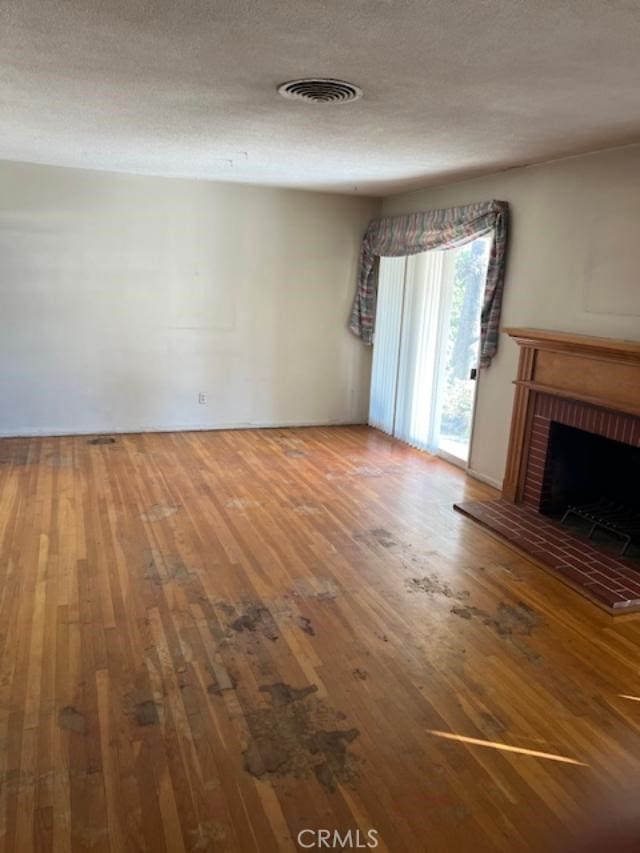 unfurnished living room featuring hardwood / wood-style floors, a textured ceiling, and a brick fireplace