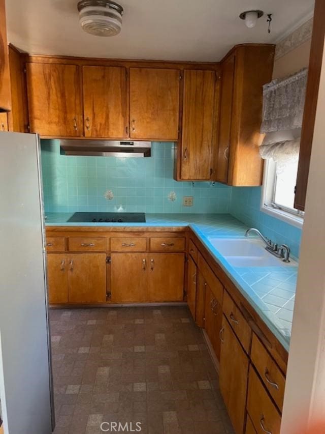 kitchen with black electric stovetop, refrigerator, sink, and tasteful backsplash