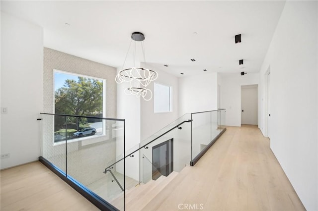 hallway with light wood-type flooring, an upstairs landing, and an inviting chandelier