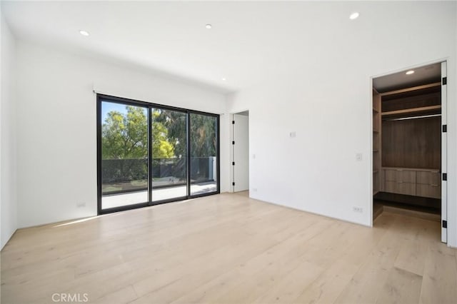 unfurnished bedroom with access to outside, a walk in closet, light wood-style flooring, and recessed lighting