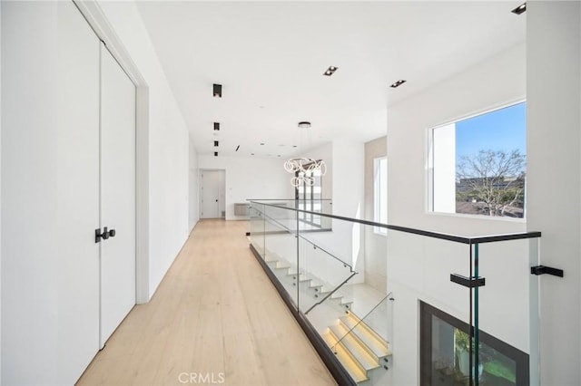 hall featuring light wood-type flooring, an upstairs landing, and a notable chandelier